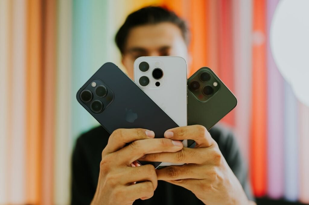 A man holds three smartphones in front of a vibrant, multicolored backdrop.